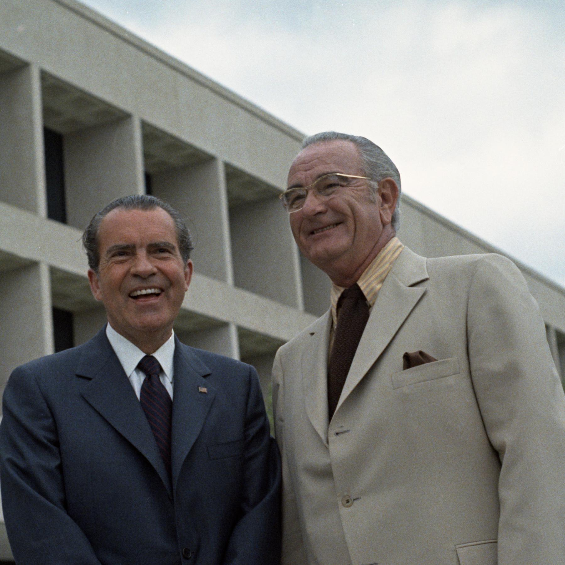 Lady Bird Johnson, Richard Nixon, and LBJ stand outside the LBJ Presidential Library with two lines of square, recessed windows tapering off to the bottom right. 